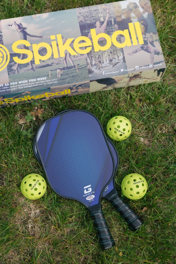 Pickleball paddles and balls placed on the grass near outdoor games